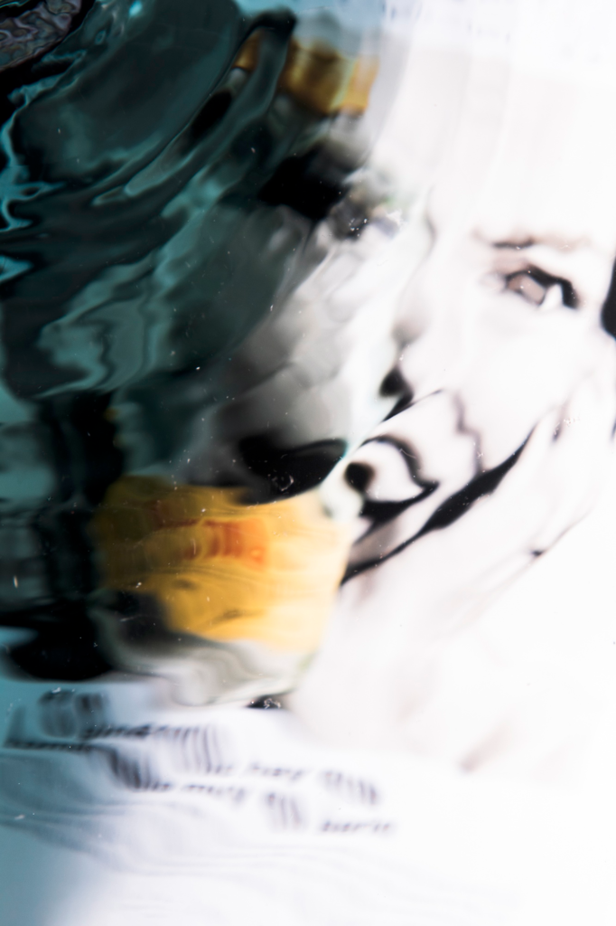 A distorted image of a face seen through a water-like reflective surface, blending abstract patterns with light and shadow.