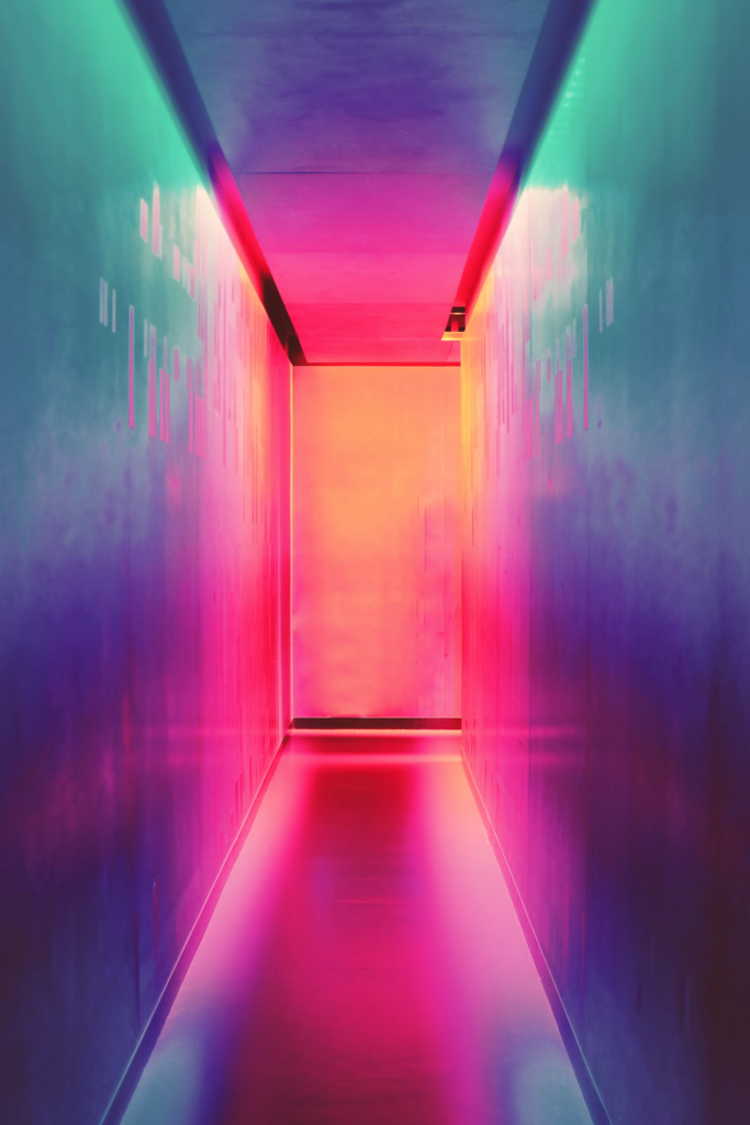 A futuristic corridor illuminated by vibrant neon colors, transitioning from pink to blue and green hues.